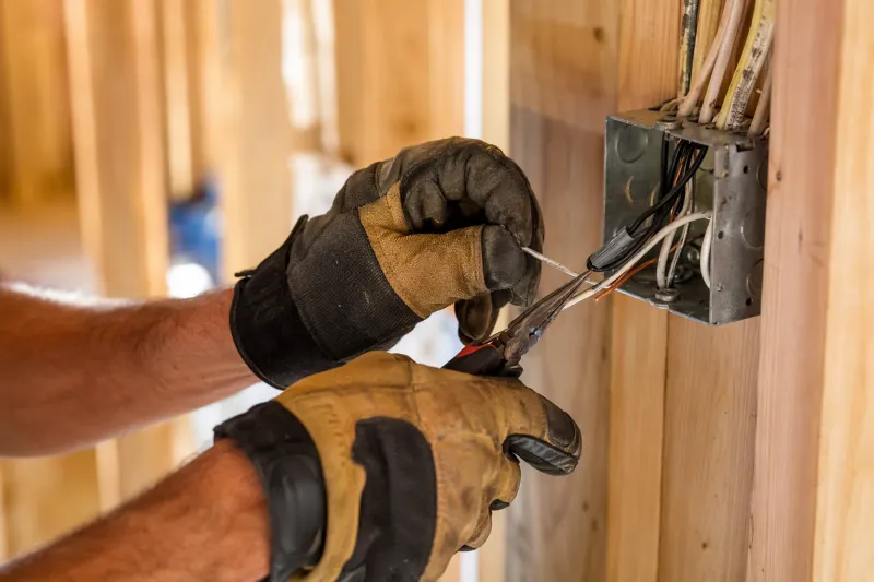 Electrician hands working carefully with wire strippers on copper lines in a junction box